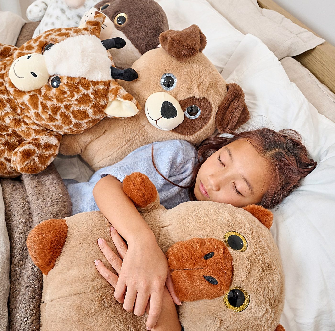 A sleeping child tucked in among giraffe, dog and bear plush toys