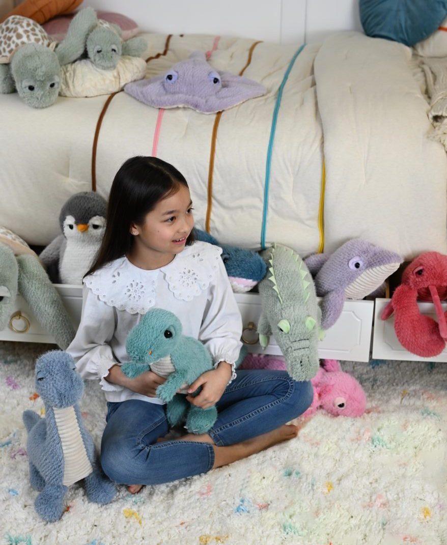 A girl on a rug with rounded Scoopz plush toys in pastel colours