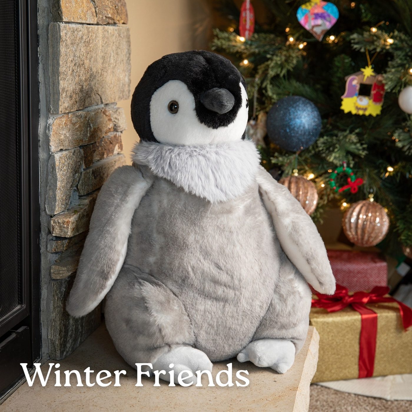 A penguin plush toy standing beside a decorated Christmas tree