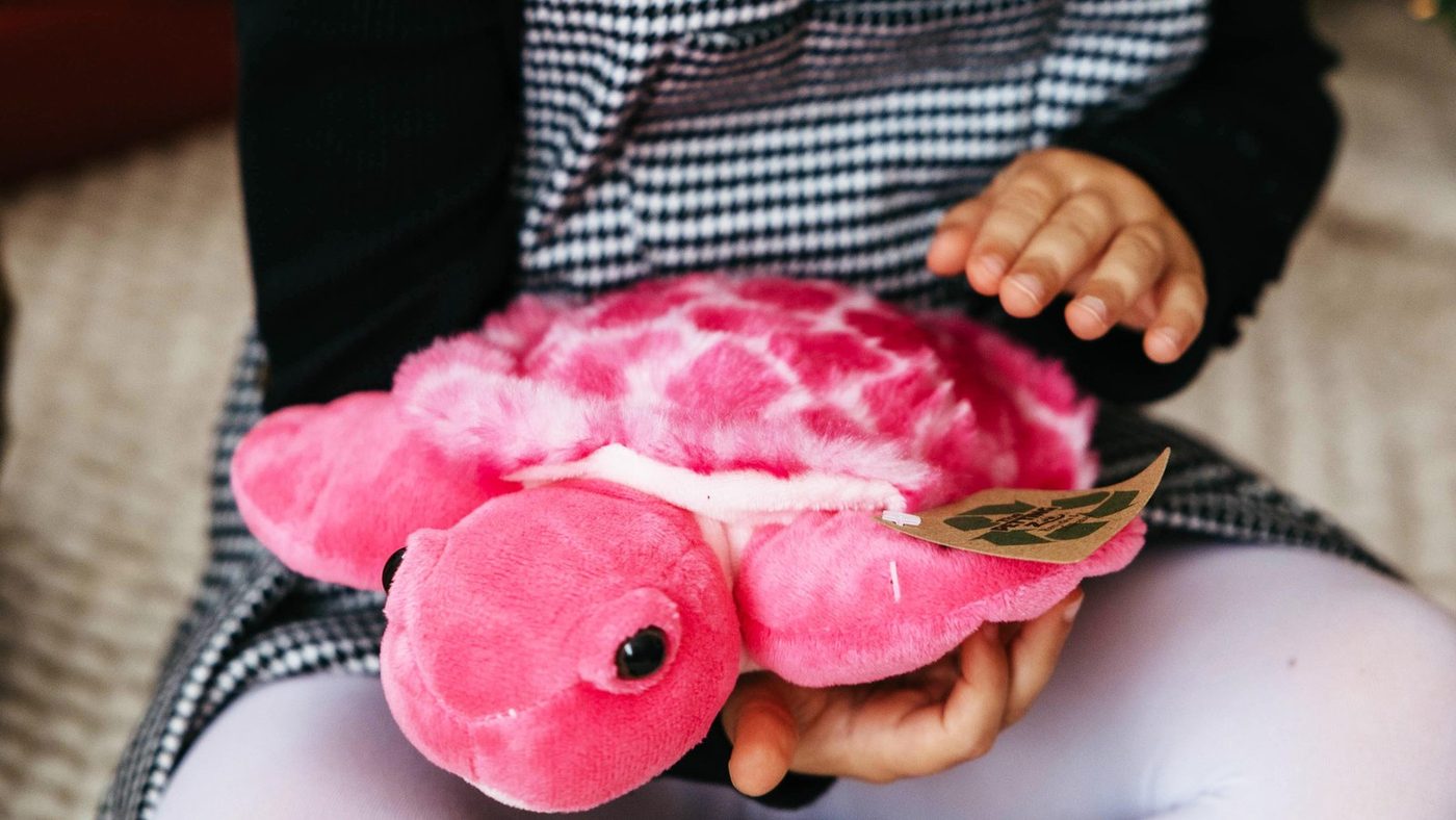 A pink axolotl jumbo plush toy lying across a child's lap