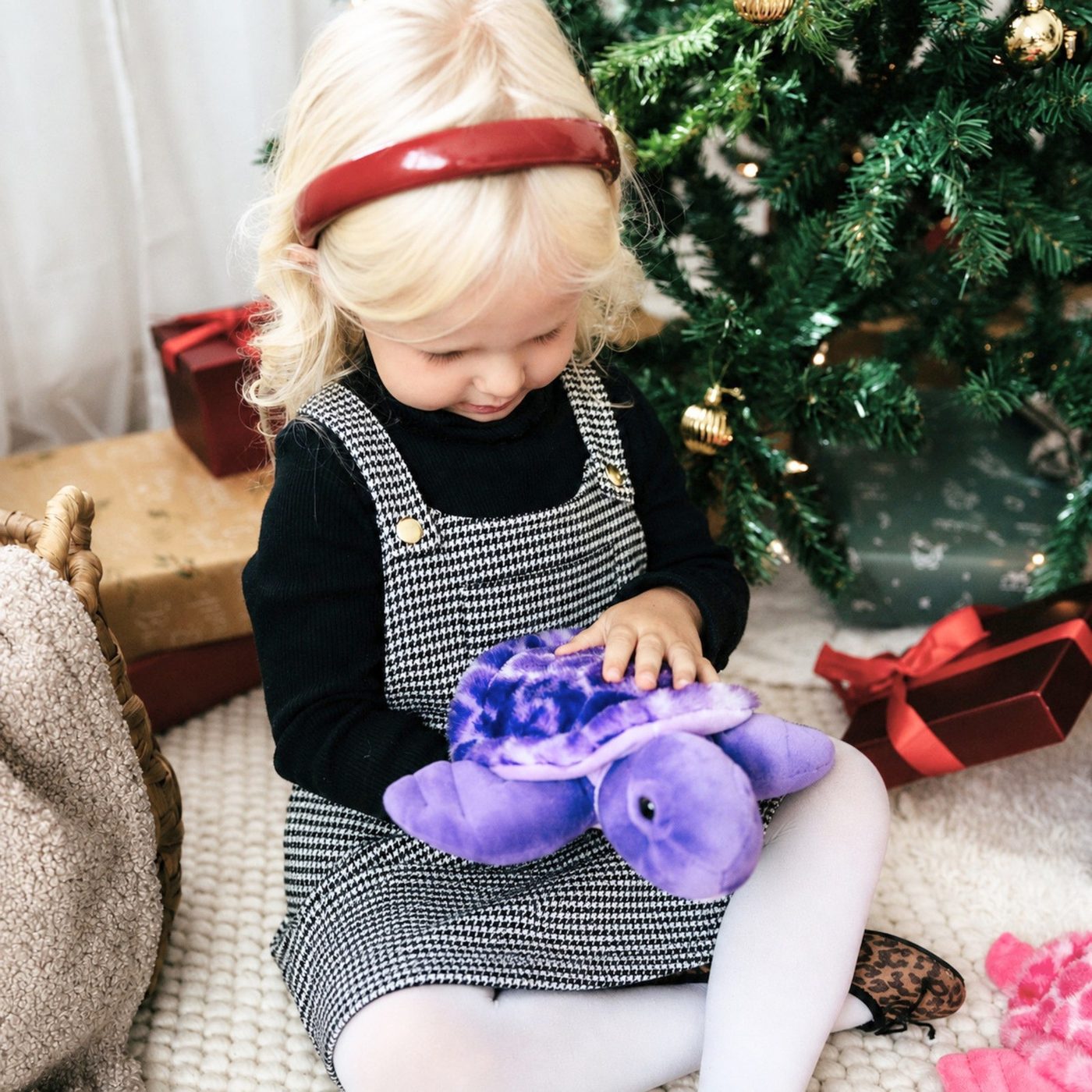 A toddler in a pinafore opening a purple plush toy at Christmas